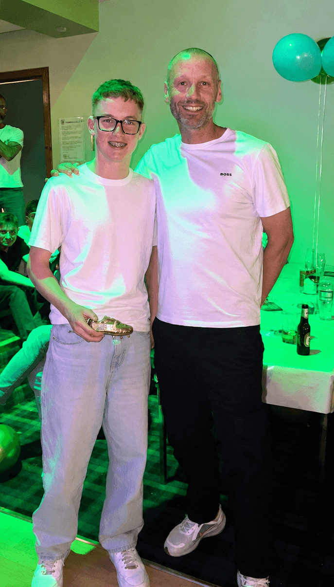 A young award recipient holding a trophy with a Spartinios coach
