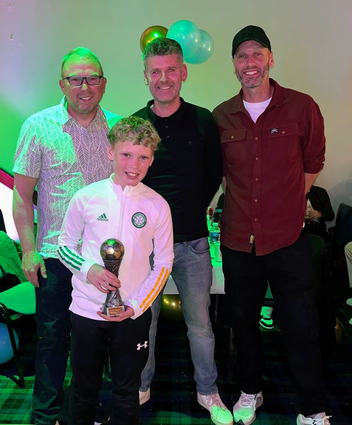 A young award recipient holding a football trophy with Spartinios coaches