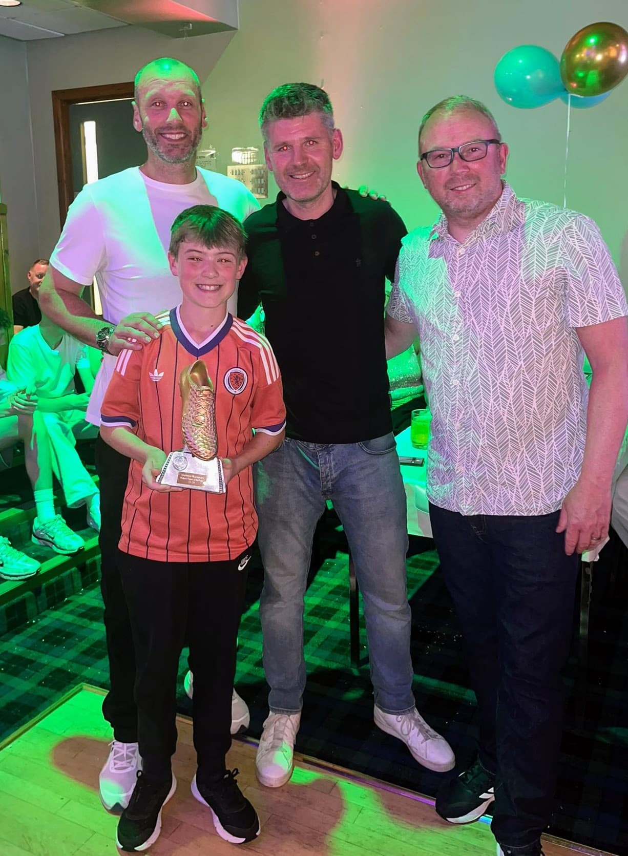 A young award recipient holding a golden boot trophy with coaches