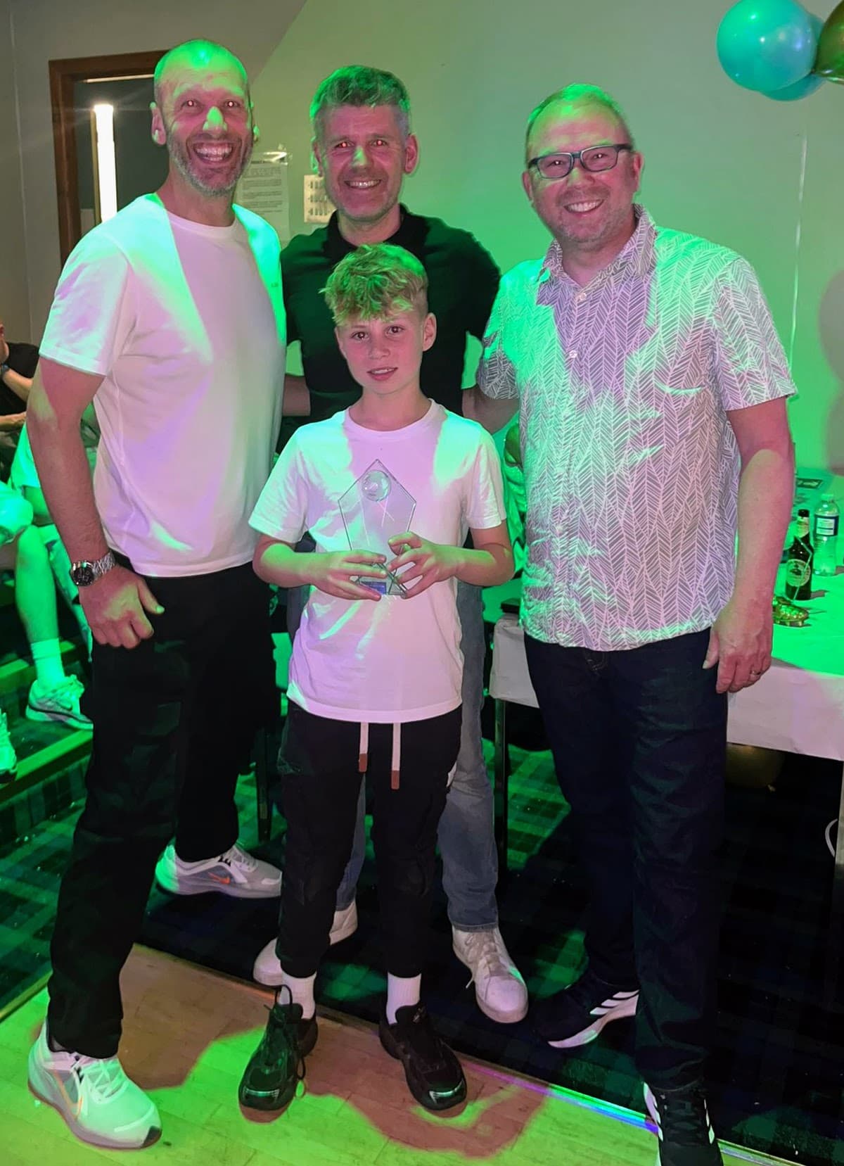 A young award recipient holding a glass trophy with coaches