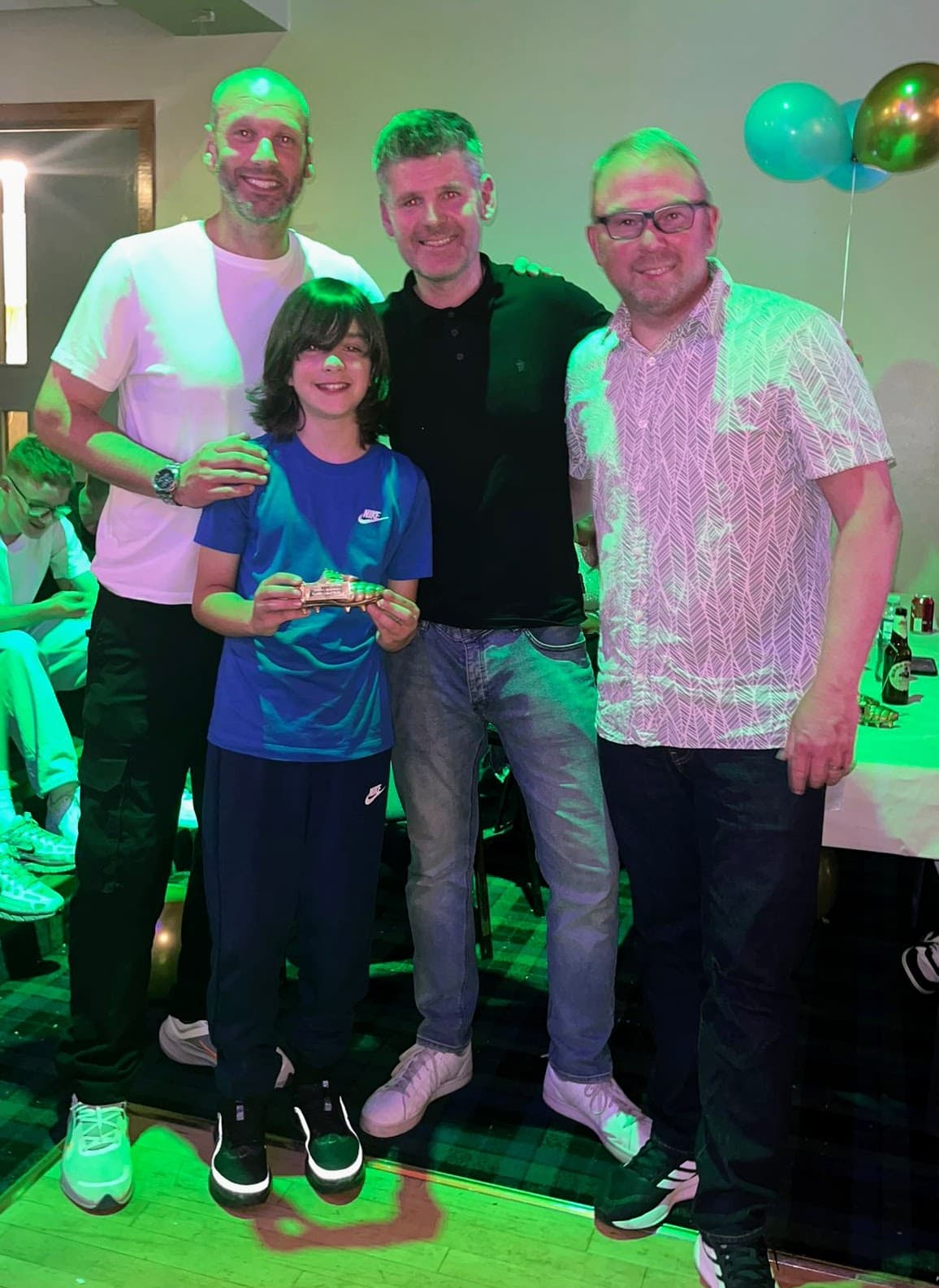 A young award recipient holding a golden boot trophy with coaches