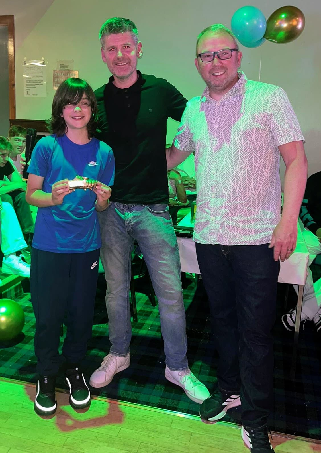 A young award recipient holding a golden boot trophy with coaches