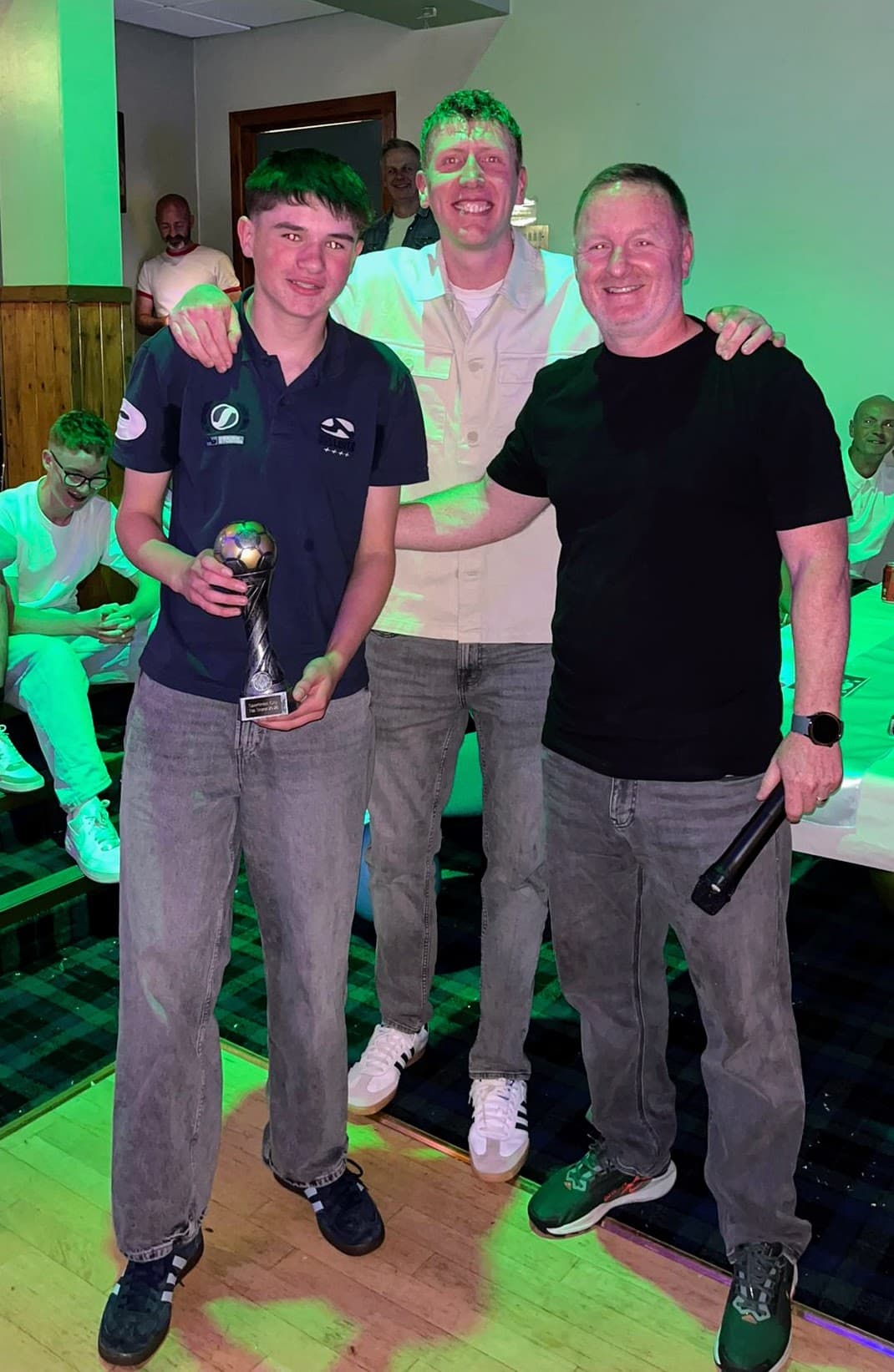 A young award recipient holding a football trophy with coaches