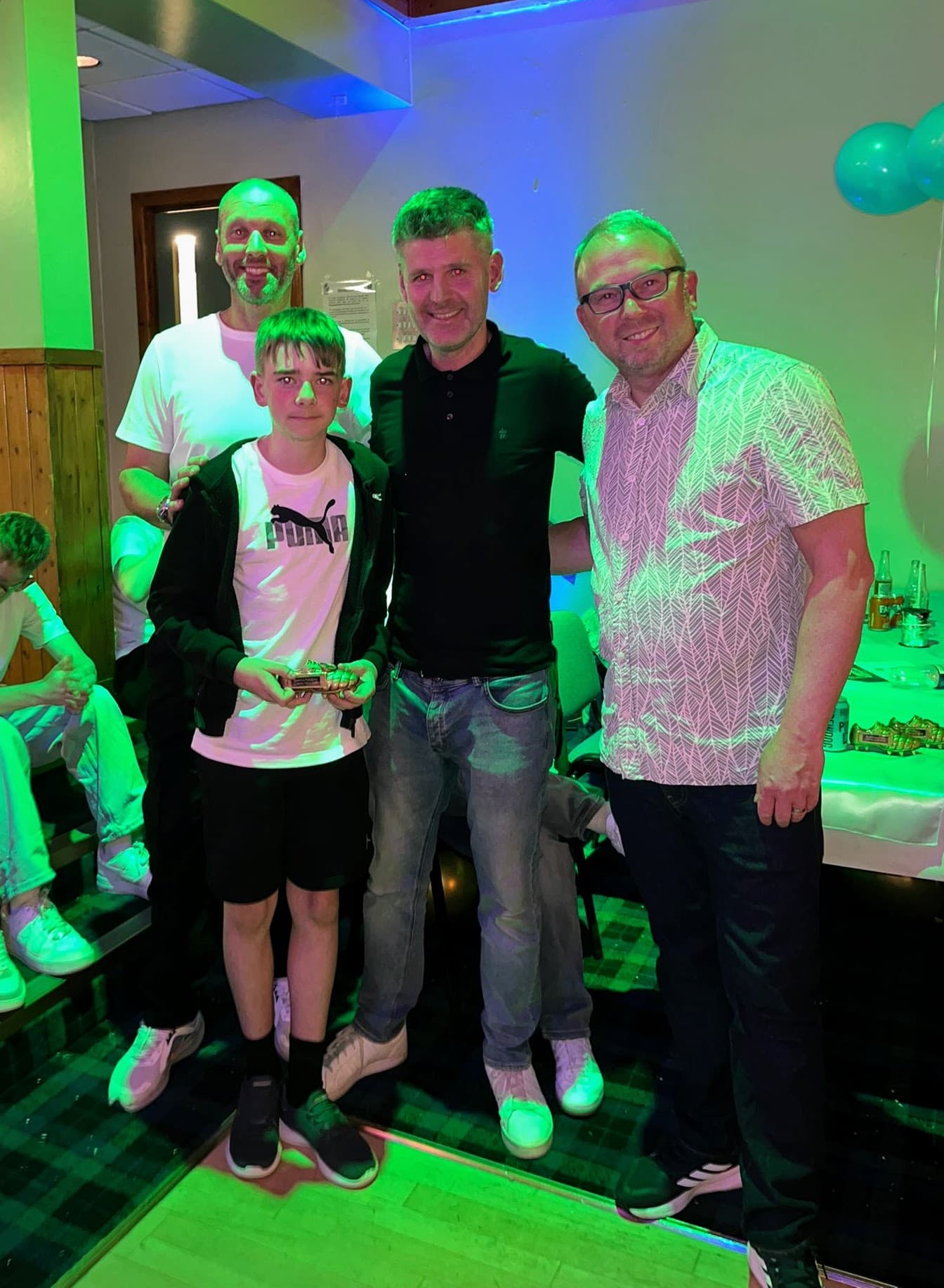 A young award recipient holding a golden boot trophy with coaches